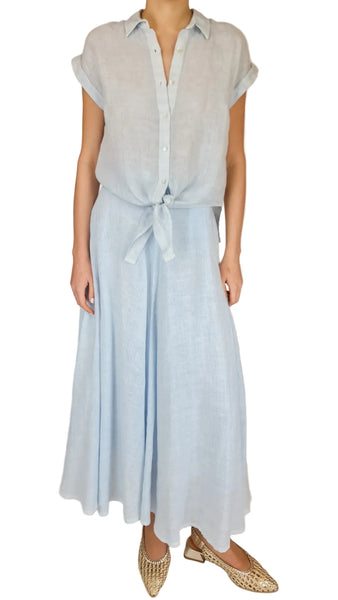 Person wearing a light blue outfit with a shirt and long skirt on a plain background