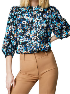 A model wearing a floral blouse with pintucking, self-button loops, and shirred shoulders paired with brown trousers.