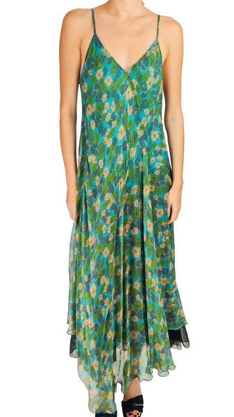 A woman modeling a sleeveless, V-neck maxi dress with thin spaghetti straps and an all-over abstract floral print in green, teal, blue, and beige, set against a plain white background.