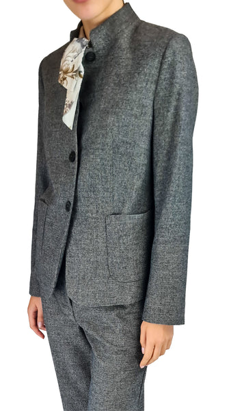 A person wearing a tailored gray textured suit jacket and matching trousers, with a patterned white neck scarf, against a plain white background.