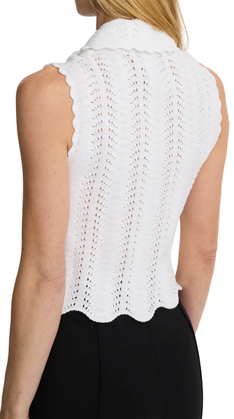 Woman wearing a white sleeveless knitted top against a plain background