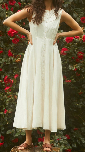 Woman in a white dress standing in front of a bush with red flowers