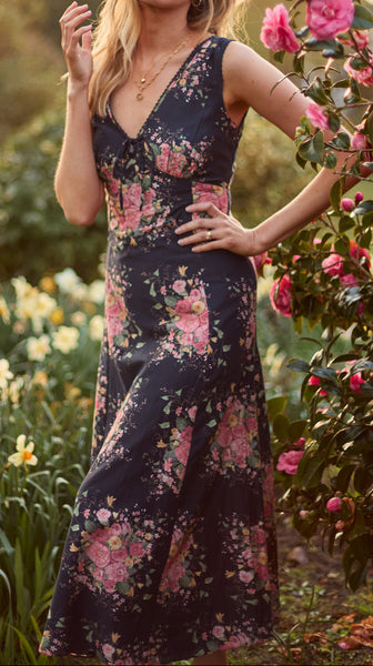 Woman in a floral dress standing in a garden with flowers around her