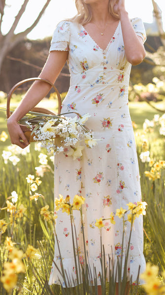 Woman in a floral dress standing in a field of daffodils with sunlight filtering through.