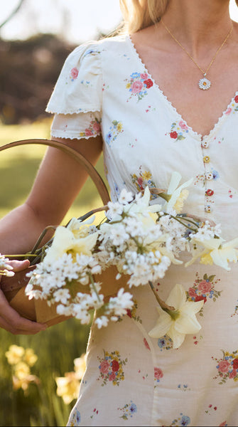 Woman in a floral dress holding flowers and a basket in a natural setting