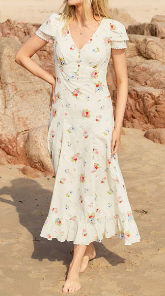Woman in a floral dress standing on a beach with rock formations in the background