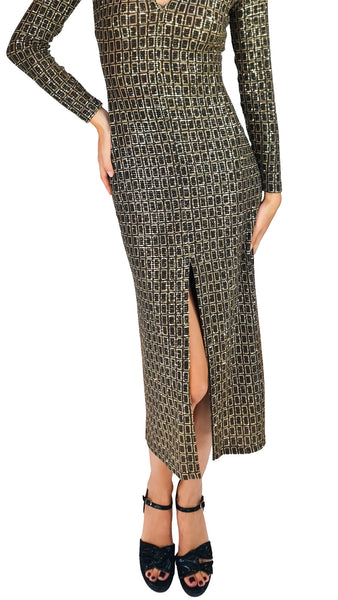 A long-sleeve midi dress with a geometric black and gold pattern, featuring a thigh-high front slit and a V-neckline, modeled with black strappy heels against a white background.