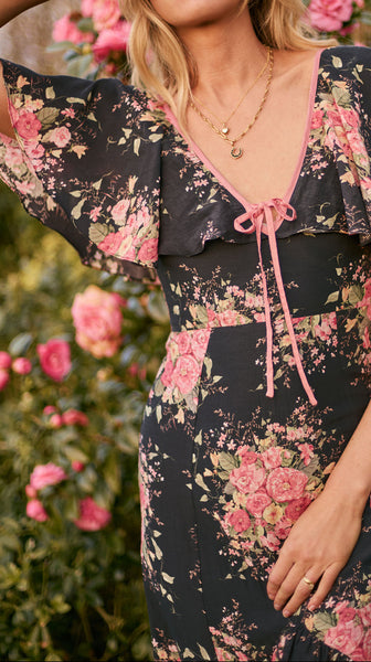 Woman wearing a floral dress with pink flowers in a garden setting
