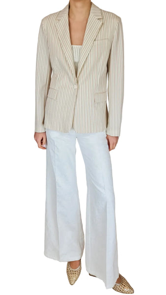 Person wearing a striped blazer, white top, and white pants on a plain background
