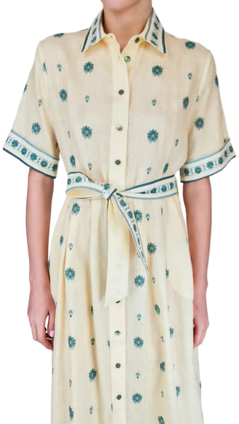 Woman wearing a yellow dress with green floral patterns on a plain background
