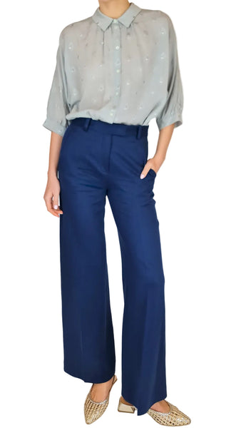 Person wearing a light blue shirt with star patterns and dark blue pants on a plain background