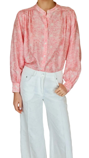 Person wearing a pink floral blouse and white pants on a plain background