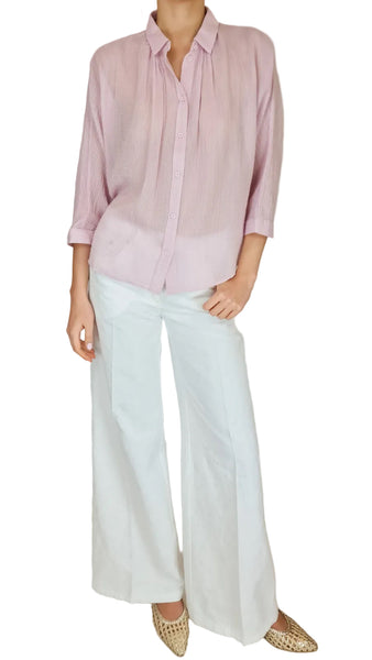 Person wearing a light pink shirt and white pants against a plain background