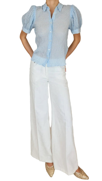 Person wearing a light blue checkered blouse and white pants on a beige background