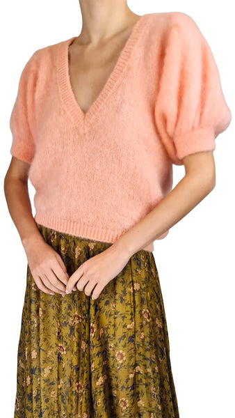 A model wearing a soft peach-pink fuzzy short-sleeve knit sweater with puff sleeves and a green floral print skirt, shown against a plain white background.