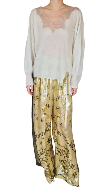 Person wearing a white top and gold pants with black patterns on a plain background