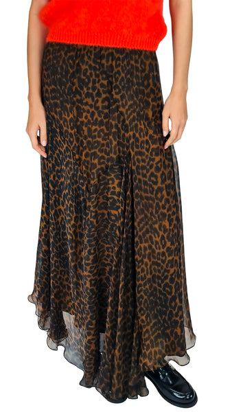 A model wearing a leopard print midi skirt in brown and black, styled with a bright orange knit top and black patent leather loafers, against a plain white background.