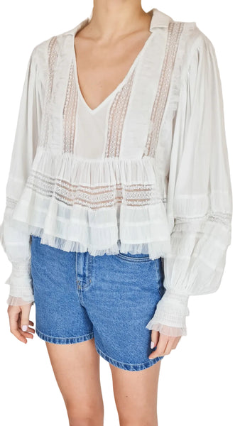 White lace blouse with long sleeves and blue denim shorts on a plain background