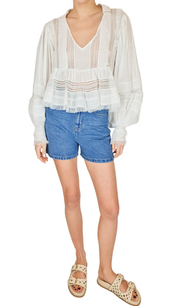 Person wearing a white blouse with ruffled sleeves and blue denim shorts on a plain background