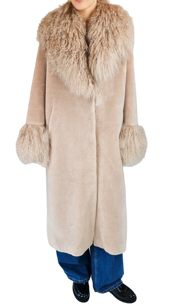 A model wearing a long beige shearling-style coat with a large shaggy faux-fur collar and matching fluffy cuffs, paired with blue jeans and black shoes, against a plain white background.
