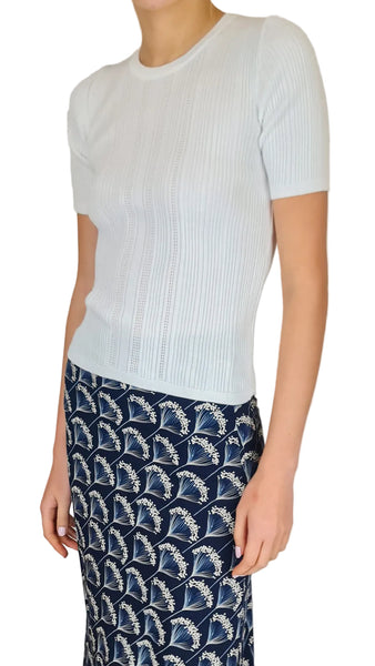 Person wearing a white ribbed sweater and navy patterned pants on a plain background