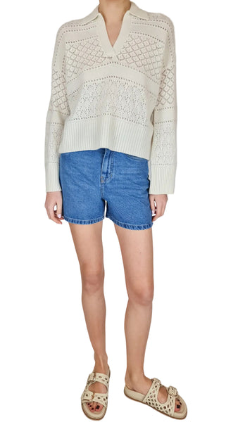 Person wearing a white textured sweater and blue shorts on a plain background