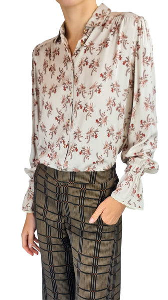 A woman wearing a cream-colored long-sleeve blouse with a red and green floral pattern, paired with dark brown and black plaid trousers, shown against a plain white background.