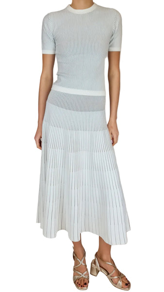 Person wearing a light blue ribbed top and pleated skirt set on a plain background