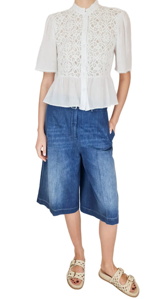 Person wearing a white lace blouse and blue denim shorts on a plain background