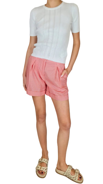 Person wearing a white sweater and pink shorts on a plain background