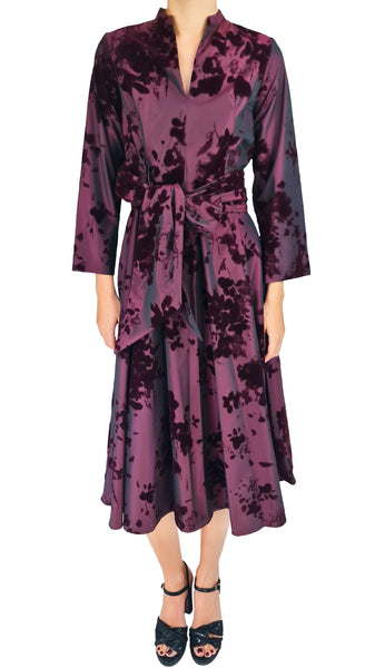 A woman modeling a long-sleeved wrap-style midi dress with a tie-dye pattern in deep purple and black, paired with black strappy heels, against a plain white background.