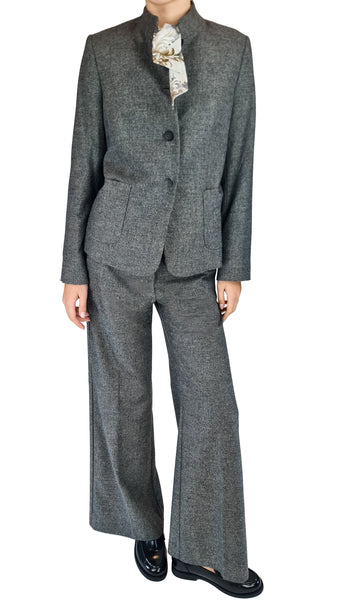 A model wearing a gray two-piece suit with a textured herringbone pattern, featuring a cropped jacket with a mandarin collar and matching wide-leg trousers, styled with a patterned cream neck scarf and black leather loafers.