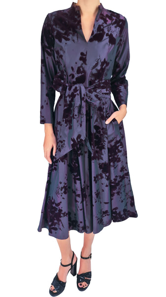 A woman modeling a long-sleeve midi wrap dress with a tie-dye pattern in dark purple and black, paired with black strappy heels, against a plain white background.