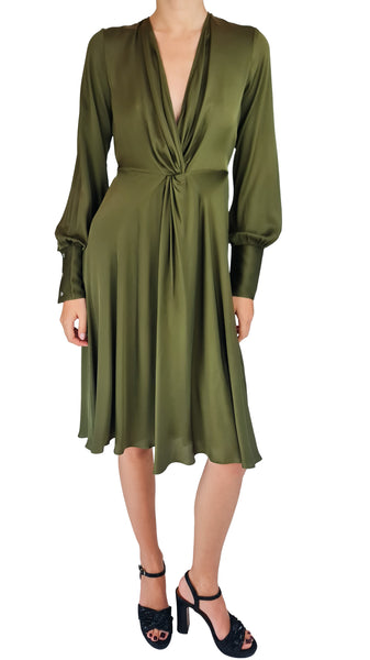 An olive green satin long-sleeve midi dress with a twisted waist and deep V-neckline, modeled with black strappy high-heeled sandals against a plain white background.