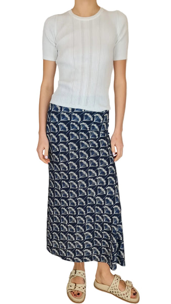 Person wearing a white sweater and navy patterned skirt on a plain background