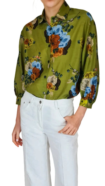 Person wearing a green floral blouse with white pants on a plain background