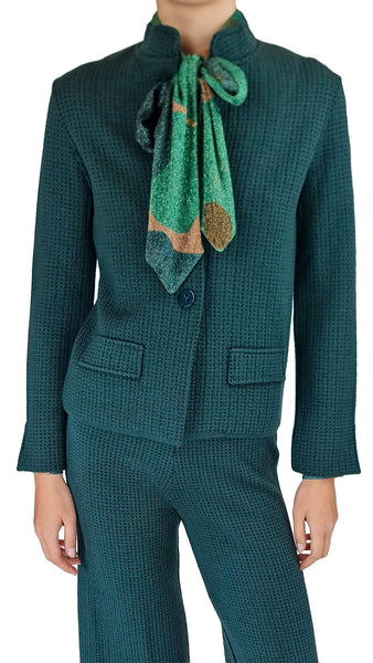 A person wearing a textured dark teal matching jacket and trousers set, accessorized with a green patterned neck scarf, against a plain white background.