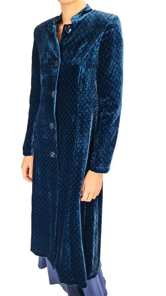 A long navy blue velvet coat with a subtle geometric pattern, featuring a stand collar and front buttons, shown on a model against a white background.