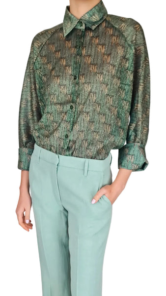 Person wearing a green patterned shirt and light blue pants on a plain background