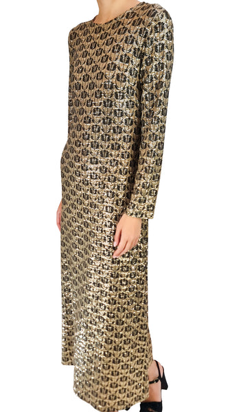 A long-sleeve maxi dress with a metallic gold and black repeating monogram pattern, shown on a model against a plain white background.