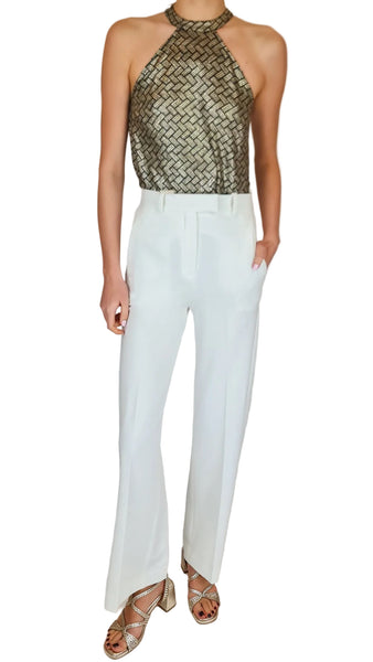Person wearing a metallic halter top and white pants on a plain background