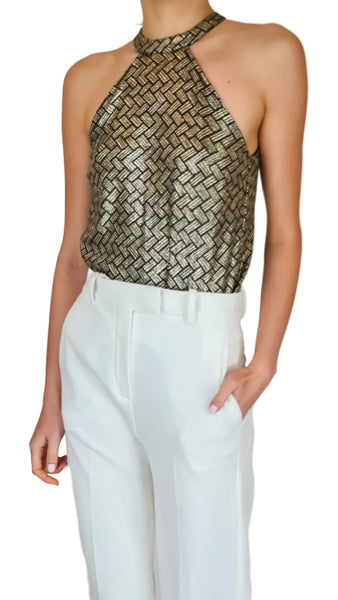 Person wearing a metallic halter top and white pants on a plain background