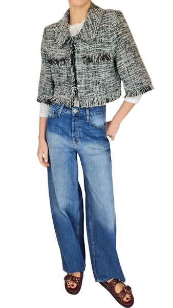 Person wearing a tweed jacket, white shirt, blue jeans, and brown sandals on a plain background