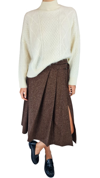 A model wearing a cream cable-knit mock-neck sweater and a brown textured pleated wrap skirt with side slits, paired with black loafers, against a plain white background.