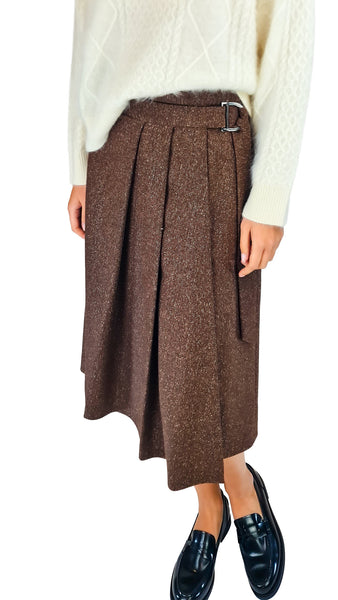A brown pleated wool skirt with a matching belt and silver buckle, styled with a cream cable-knit sweater and black loafers, shown on a model against a white background.