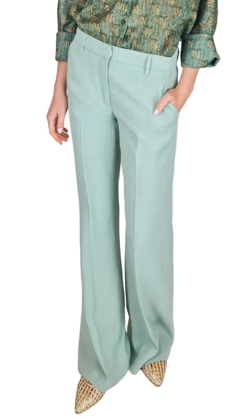Person wearing light green pants with a patterned top on a plain background
