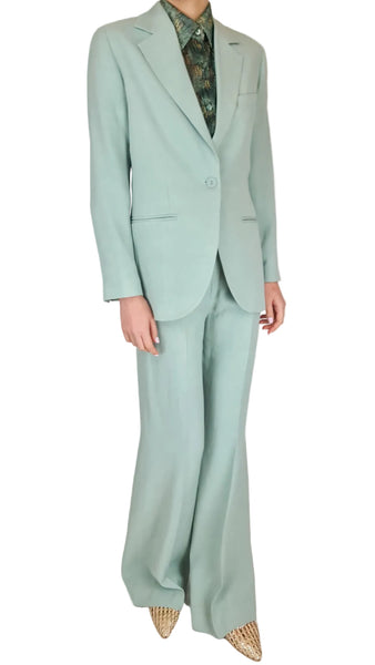 Person wearing a light blue suit with a patterned shirt on a plain background